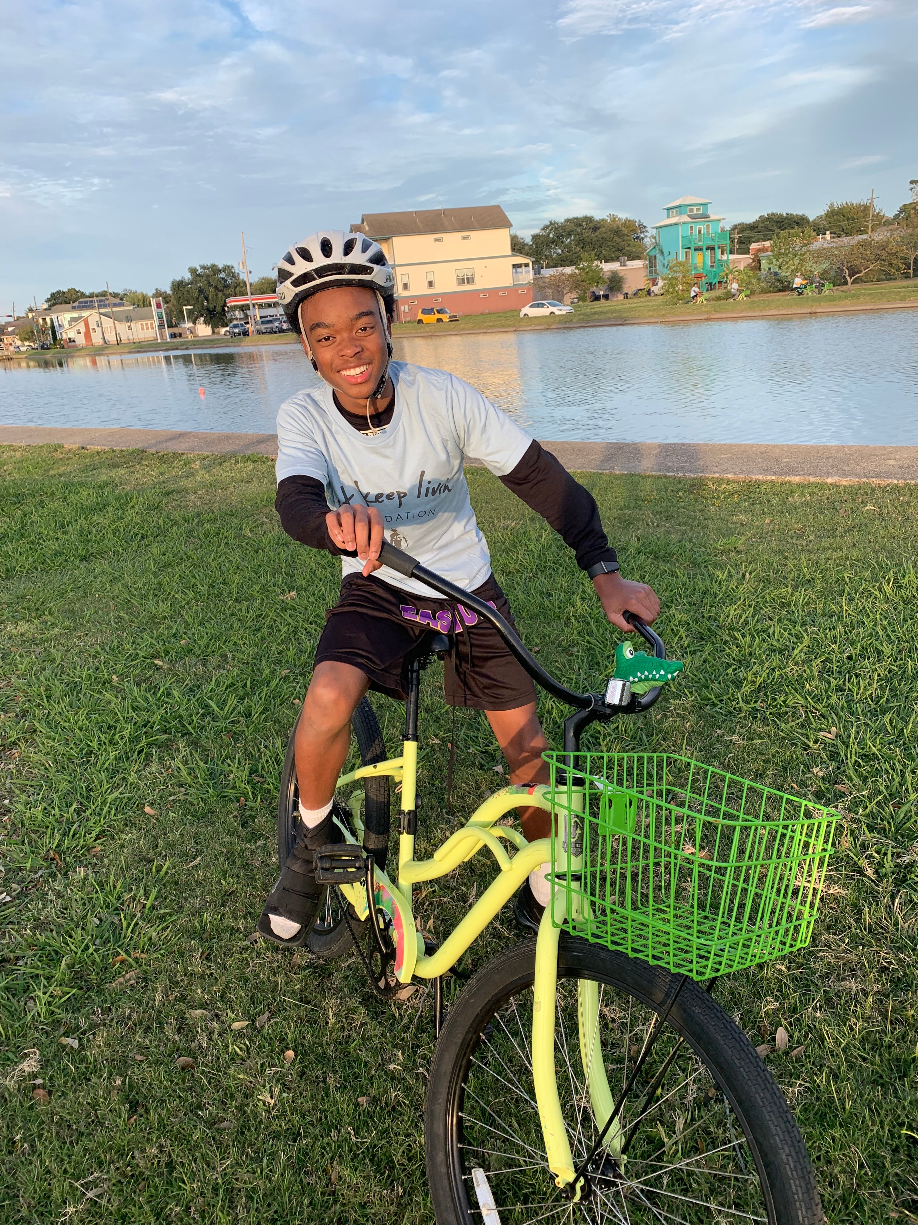 Person lying on a bicycle with a green basket in a grassy area by a water body.