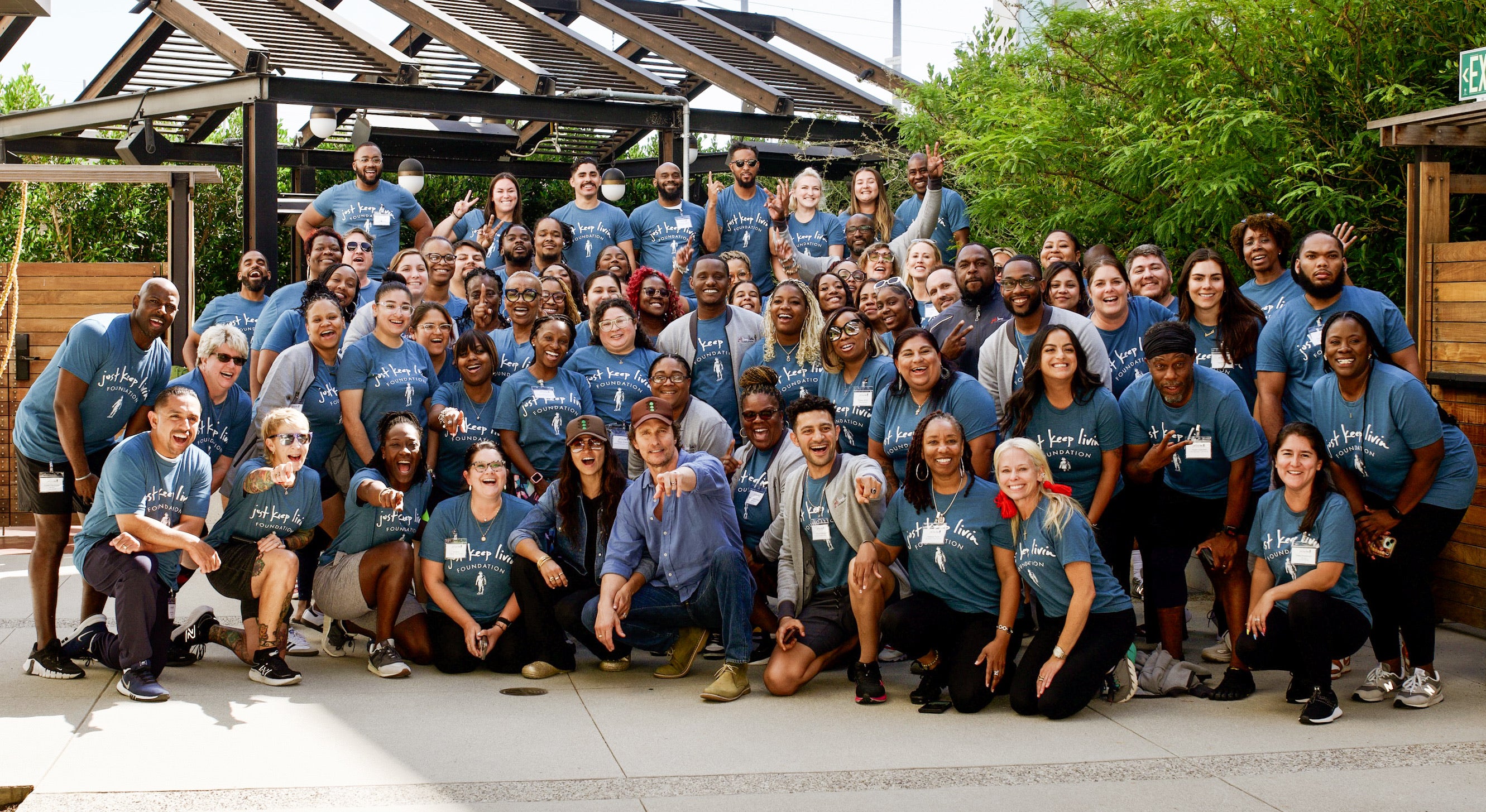 Group of Just Keep Livin students and supporters  with Matthew and Camila McConaughey wearing matching blue Just Keep Livin shirts in an outdoor setting. 
