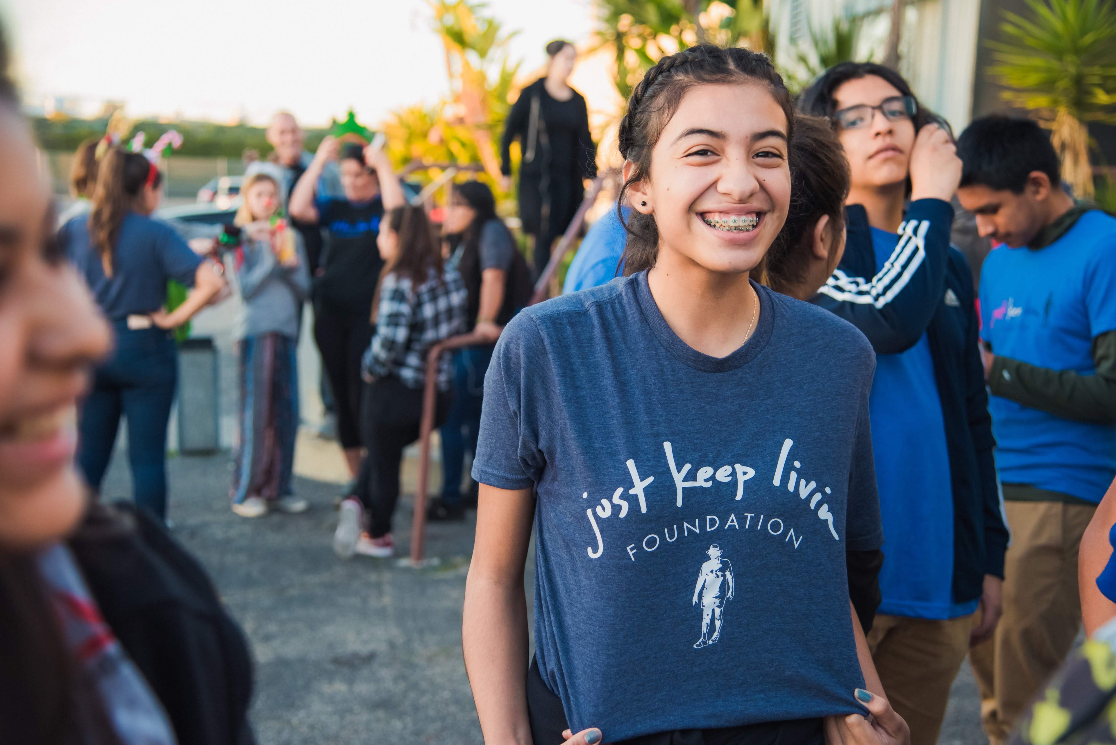 Person wearing a blue 'just keep livin' FOUNDATION' t-shirt among a crowd.