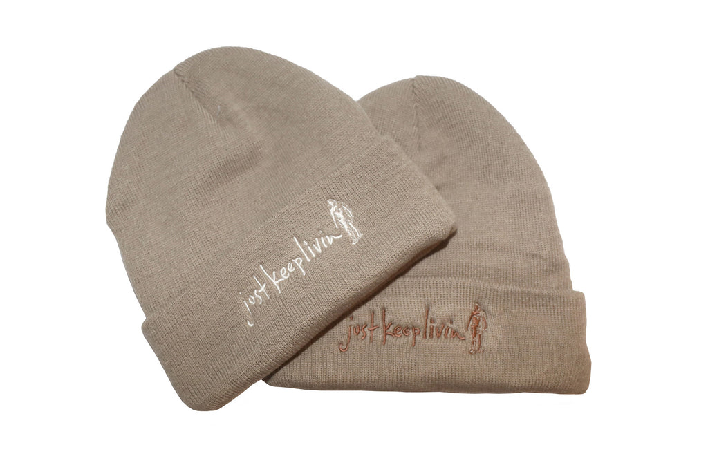 Two light tan fleece-lined beanies with embroidered text on the cuff, one displayed upright and the other turned sideways.
