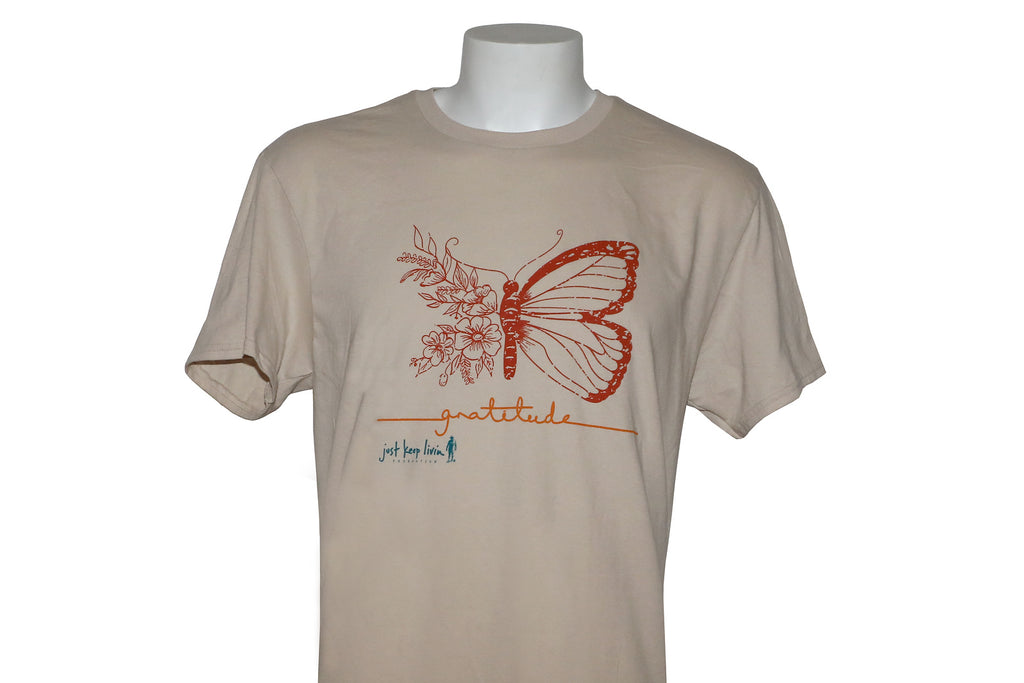 A light tan colored t-shirt with a graphic design of a butterfly and the phrase 'GRATITUDE IS THE ATTITUDE' printed on the front.