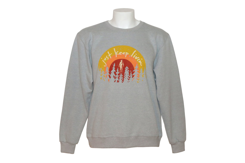 Light gray sweatshirt with Just Keep Living sunrise logo with tree silhouette background on bottom of logo. 