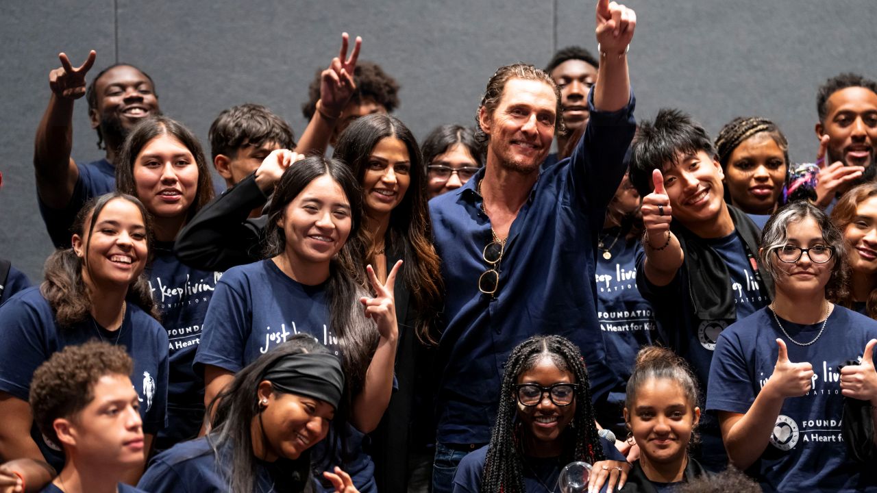 Matthew and Camila McConaughey posing with Just Keep Livin students wearing dark blue shirts with Just Keep Living Foundation logo. 