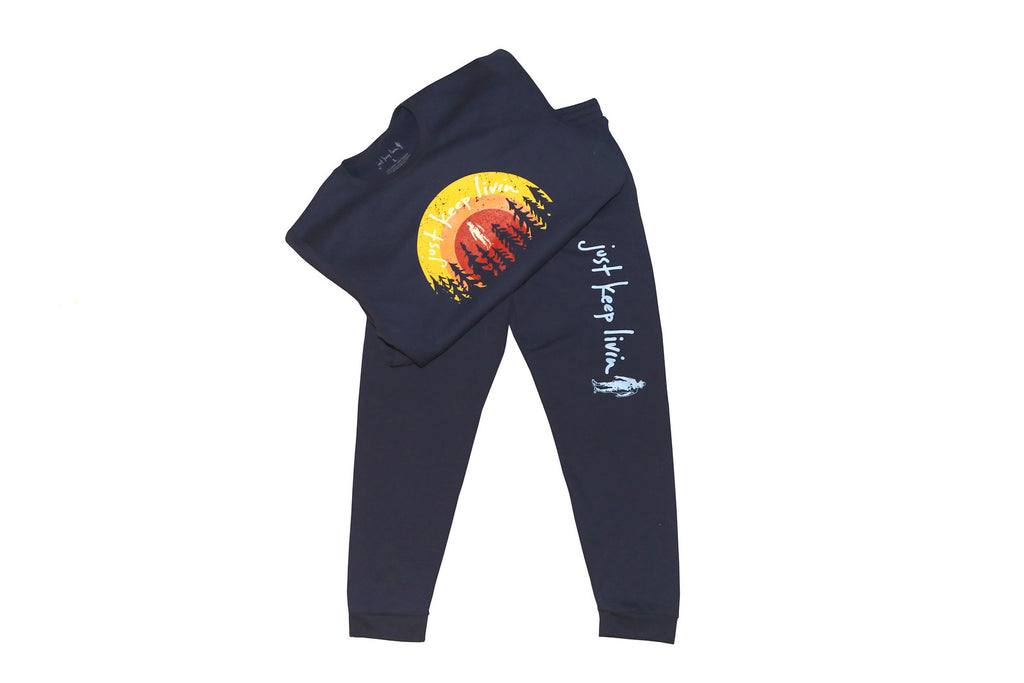 Navy blue jogging sweatshirt and pant set. sunrise yellow, orange, and red just keep livin logo with tree backdrop on sweatshirt. just keep livin text logo on left pant leg above knee. 