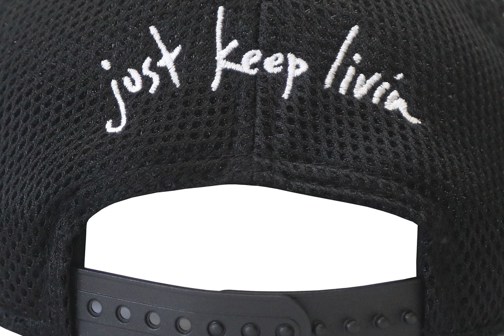 Close up of back of black snap back hat with white just keep livin embroidery. 