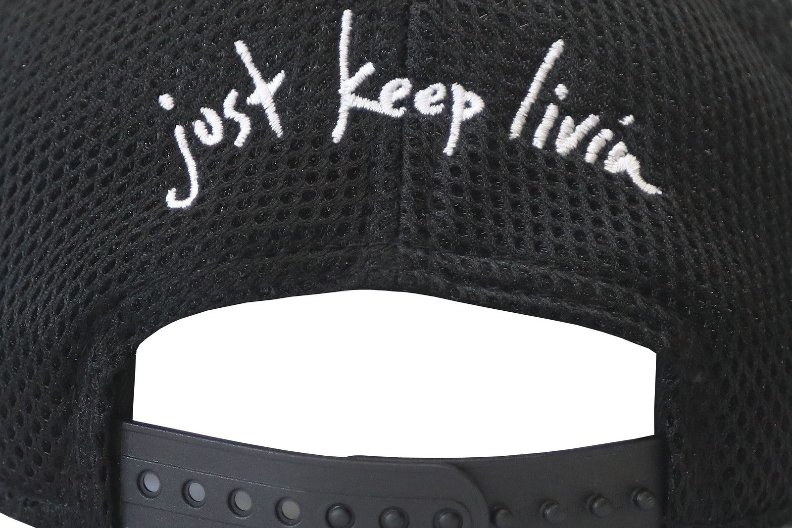 Close up of back of black snap back hat with white just keep livin embroidery. 