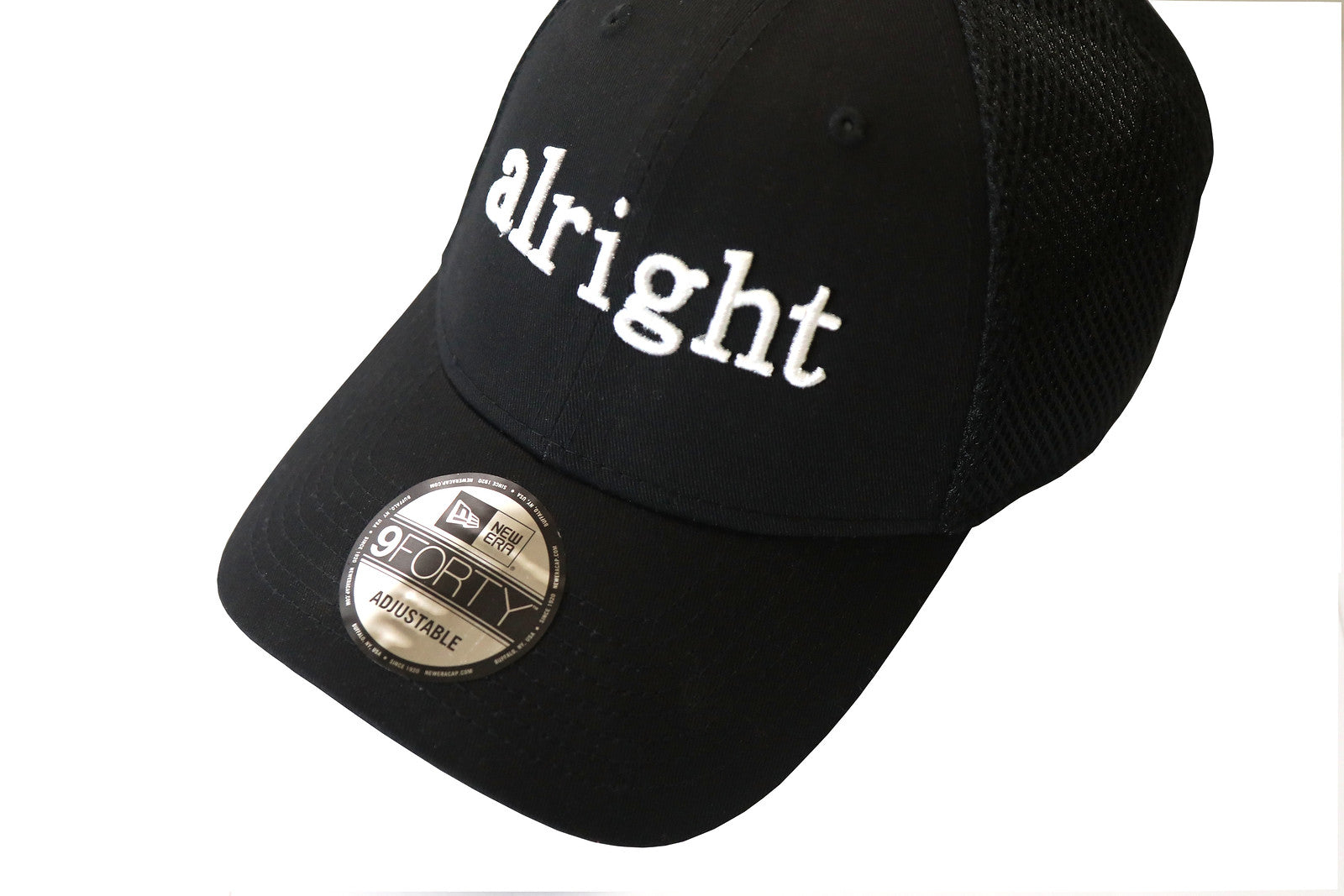 A black baseball cap with the word 'Alright' embroidered in white on the front and a gray mesh back panel.